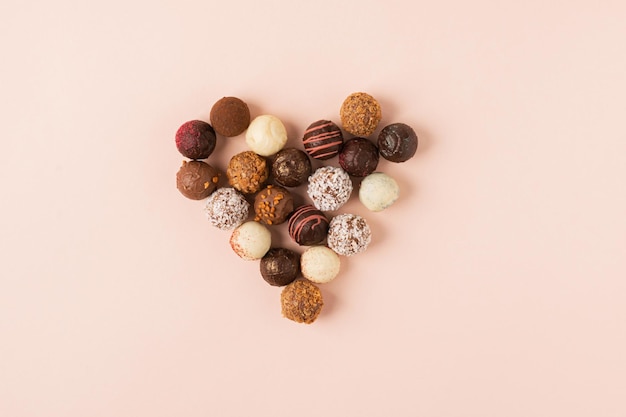 Bonbons à la truffe au chocolat avec différents coeurs remplissant un fond rose pastel