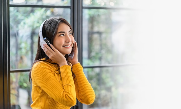 Bonheur asiatique souriante jeune femme portant des écouteurs sans fil technologiques pour écouter de la musique