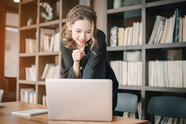 Bonheur confiant jeune femme travaillant sur un ordinateur portable ou un cahier dans son bureau.