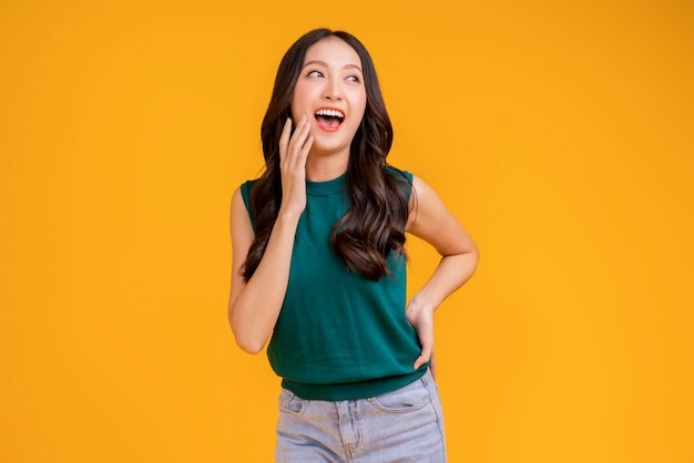 Bonheur décontracté femme asiatique souriante joyeuse en t-shirt vert bleu jean se détendre paisible pensée positive mode de vie insouciant debout geste de la main expression du visage avec un fond de couleur jaune