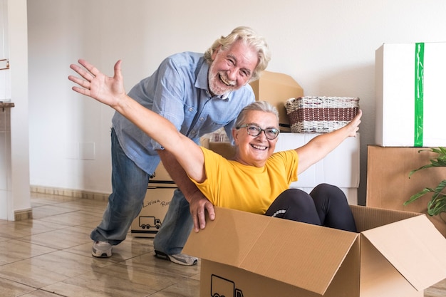 Bonheur de deux personnes âgées dans une pièce vide jouant comme des enfants en déménagement heureux d'un nouveau départ comme à la retraite avec des cartons de déménagement sur le sol