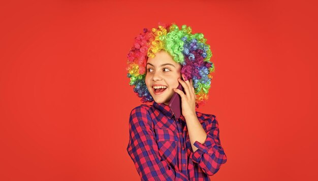 Bonheur de l'enfance positif et joyeux enfant regardant drôle dans la teinture des cheveux de la perruque arc-en-ciel chez le coiffeur enfant s'amusant joyeux anniversaire fête petite fille perruque colorée parler au téléphone