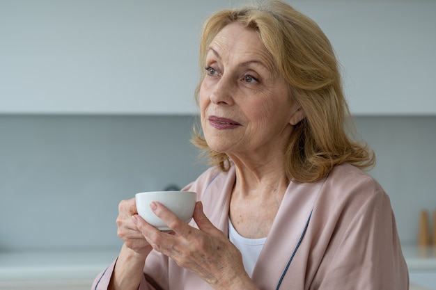 Le bonheur d'une femme âgée en peignoir buvant du café le matin en rêvant