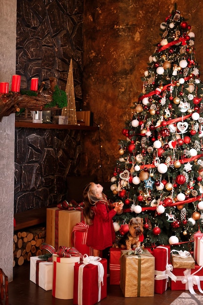 Bonheur de Noël petite fille heureuse et chien près d'un immense sapin de Noël avec des cadeaux de Noël en famille