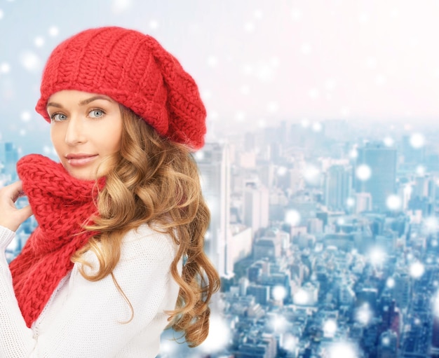 Photo bonheur, vacances d'hiver, noël et concept de personnes - jeune femme au chapeau rouge et écharpe sur fond bleu neigeux