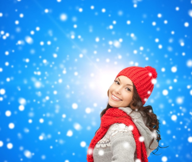 bonheur, vacances d'hiver, noël et concept de personnes - jeune femme souriante au chapeau rouge et écharpe sur fond bleu neigeux