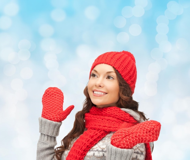 bonheur, vacances d'hiver, noël et concept de personnes - jeune femme souriante au chapeau rouge, écharpe et mitaines sur fond de lumières bleues