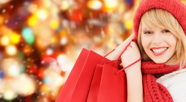 bonheur, vacances d'hiver, noël et concept de personnes - jeune femme souriante en bonnet et écharpe avec des sacs à provisions sur fond de feux rouges