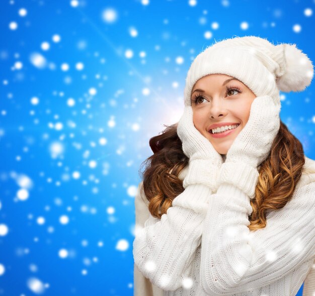 bonheur, vacances d'hiver, noël et concept de personnes - jeune femme souriante en chapeau blanc et mitaines sur fond bleu neigeux