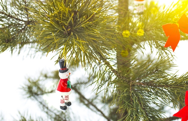 Bonhomme de neige et arcs rouges sont accrochés au pin de Noël. Photo naturelle dans la forêt gelée. Carte postale de joyeuses fêtes. Décoration d'ornements du nouvel an. Temps de neige.