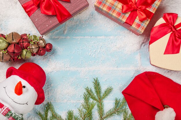 Bonhomme de neige avec coffrets, branche de sapin, bonnet de Noel sur une surface en bois bleue enneigée