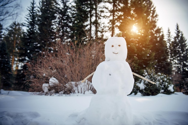 Bonhomme de neige dans la forêt d'hiver ensoleillée contre les arbres et la neige blanche. Nouvel An, jeux actifs en plein air.