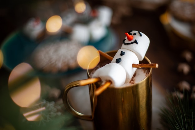 Un bonhomme de neige en guimauve décoré de glaçage doré mug avec cacao et décor de noël pain d'épice dans le...