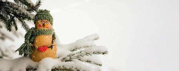 Photo bonhomme de neige, jouet sur fond d'arbre de noël enneigé. il neige. mise au point sélective, arrière-plan flou d'hiver. le concept de la nouvelle année à venir.