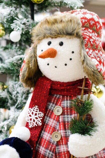 Un bonhomme de neige jouet se tient près d'un arbre de Noël dans un centre commercial. Photo verticale