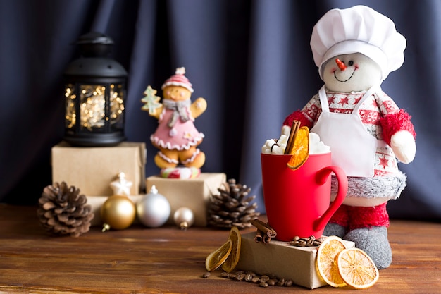 Un bonhomme de neige et une tasse givrée rouge avec des guimauves et de la cannelle sur fond de Noël