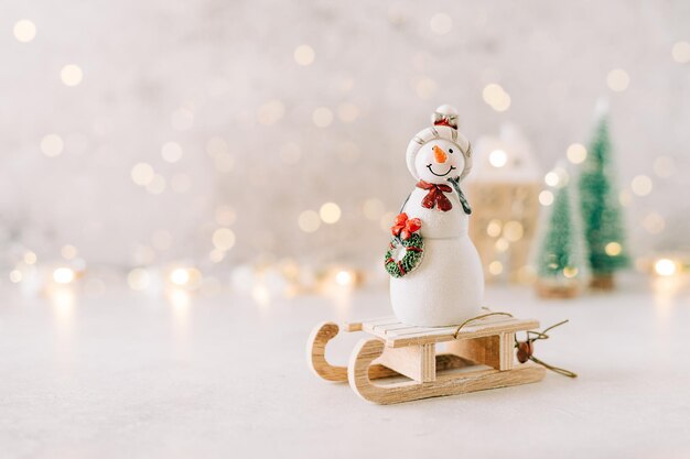 Bonhomme de neige sur traîneau en bois jouet sur fond gris avec lumière rougeoyante bokeh copie espace carte de nouvel an noël