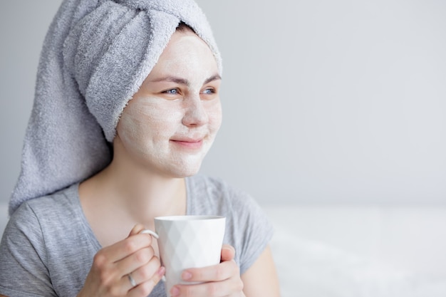 Bonjour et concept de soins de la peau - portrait en gros plan d'une belle jeune femme avec un masque facial buvant du café