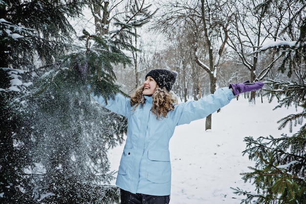 Bonjour hiver heureux hiver heureux jeune femme bouclée avec les mains levées célébrant la neige d'hiver