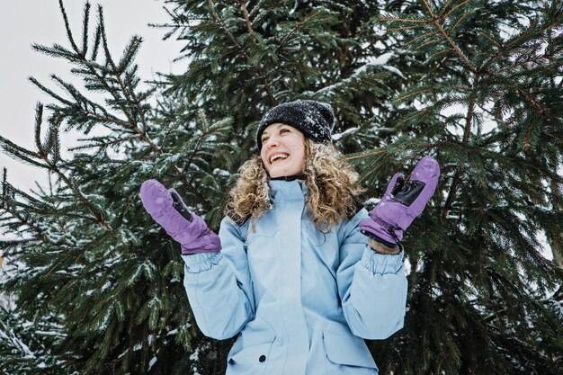 Bonjour hiver heureux hiver heureux jeune femme bouclée avec les mains levées célébrant la neige d'hiver