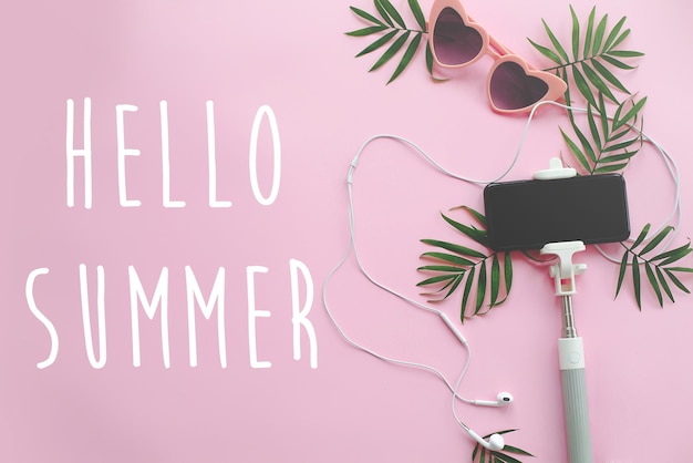 Bonjour Texte d'été sur un téléphone à lunettes de soleil rose élégant sur un casque à selfie et des feuilles de palmier vertes sur fond rose vacances d'été élégantes à plat bonjour vacances