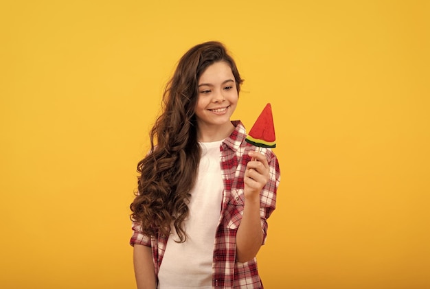 Bonne adolescente aux longs cheveux bouclés tenir des bonbons au caramel sucette sur fond jaune magasin de caramel