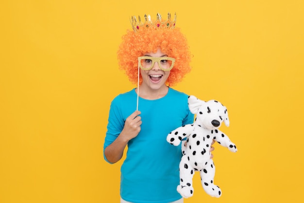 Bonne adolescente en perruque de clown fantaisie porter une couronne de reine et des lunettes de fête drôles tenir l'enfance jouet