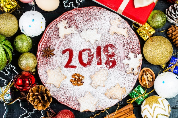 Bonne année 2018 écrit sur la farine et les décorations de Noël Biscuits de pain d&#39;épice, cannelle, oranges, épices, noix et emporte-pièces sur fond en bois. Carte de Noël, carte de voeux de nouvel an