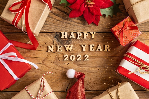 Bonne année 2022 fond festif avec lettres en bois et coffrets cadeaux artisanaux, poinsettia et bonnet de noel sur fond en bois