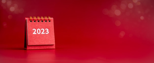 Photo bonne année 2023 bannière 2023 numéros année sur petite couverture de calendrier de bureau rouge isolé sur fond rouge avec espace de copie minimaliste prêt à commencer de nouveaux objectifs