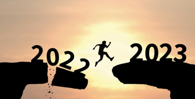 Bonne année 2023 Man silhouette jumping cliff de 2022 à 2023 sur fond de ciel nuageux