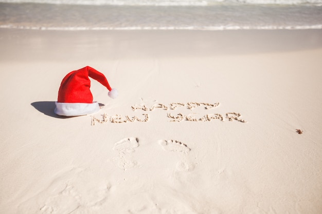 Bonne année écrit dans le sable et Santa Hat sur la plage de sable blanc