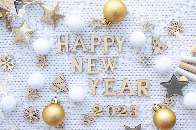 Bonne année lettres en bois et chiffres 2023 sur fond tricoté blanc festif avec paillettes étoiles lumières de guirlandes carte postale de voeux couverture de calendrier