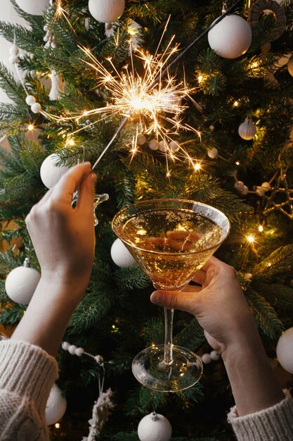Bonne année Mains tenant un cierge magique brûlant et un verre de champagne à la fête des lumières de l'arbre de Noël
