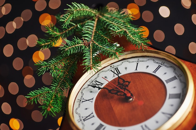 Bonne année à minuit, vieille horloge en bois avec des lumières de vacances et des branches de sapin