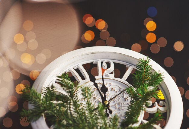 Bonne année à minuit, vieille horloge en bois avec des lumières de vacances et des branches de sapin