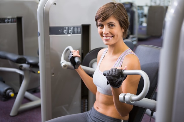 Bonne brune heureuse utilisant une machine de musculation pour les bras