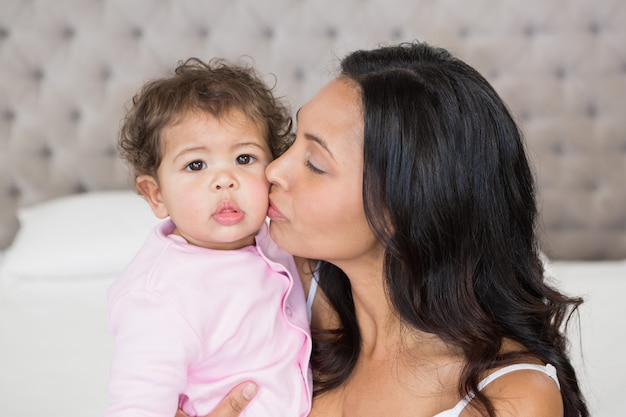 Bonne brunette embrasse son bébé sur le lit