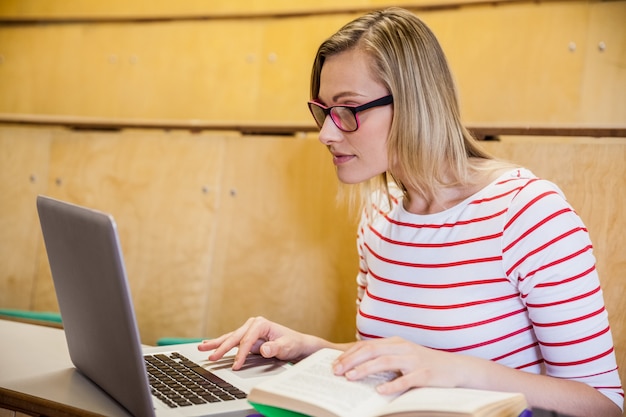 Bonne étudiante à l&#39;aide d&#39;un ordinateur portable et en lisant à l&#39;université