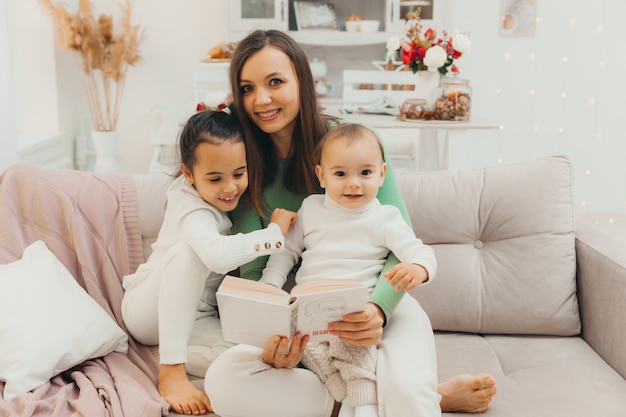 Bonne famille aimante. belle jeune maman lit un livre à ses enfants sur le canapé du salon.