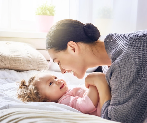 Bonne famille aimante. Une jeune mère joue avec sa petite fille dans la chambre. Maman et enfant s'amusent sur le lit.