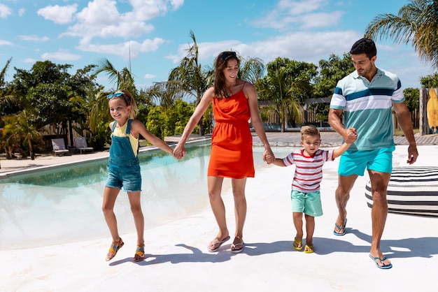 Bonne famille biraciale marchant et se tenant la main au bord de la piscine. Passer du temps de qualité, style de vie, famille, été et concept de vacances.