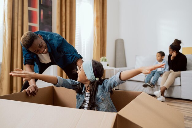 Bonne famille drôle emménageant dans un nouvel appartement fille d'âge préscolaire assise dans des boîtes en carton faisant semblant