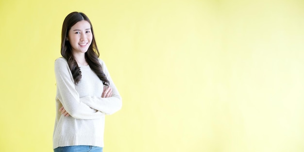 Bonne femme asiatique bras croisé souriant en se tenant debout sur fond jaune isolé