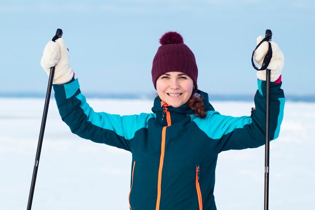 Bonne femme positive ski dans des vêtements chauds d'hiver et un chapeau à l'extérieur à une journée froide et ensoleillée