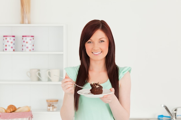 Bonne femme rousse manger un gâteau dans la cuisine