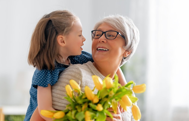 Bonne fête des mères L'enfant félicite mamie en lui donnant des fleurs Grand-mère et fille souriante