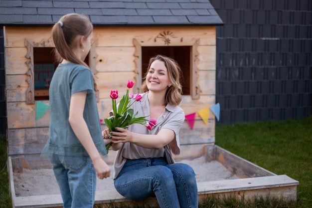 Bonne fête des mères Enfant fille félicite maman et lui donne des fleurs tulipes Maman et fille souriant et étreignant Vacances en famille et convivialité