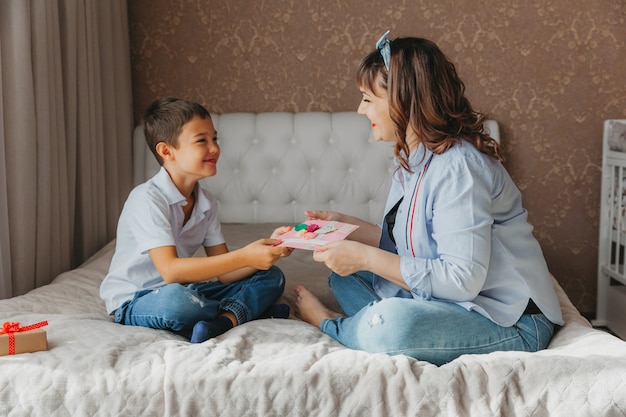 Bonne fête des mères. Fils félicite maman et donne une carte postale. Maman et bébé sourient et s'embrassent. Vacances en famille.