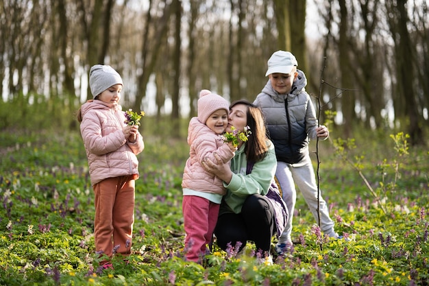 Bonne fête des mères Nous t'aimons maman Mère avec un bouquet de fleurs et trois enfants dans la forêt en fleurs de printemps